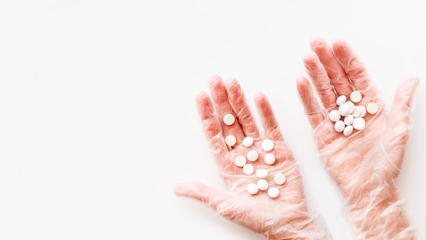 Doctor's palm hands in protective transparent gloves full of white scattering pills. Capsules with medicines on white background with copy space. Flat lay, top view.