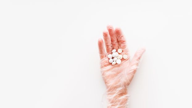 Doctor's palm hand in protective transparent glove full of white scattering pills. Capsules with medicines on white background with copy space. Flat lay, top view.