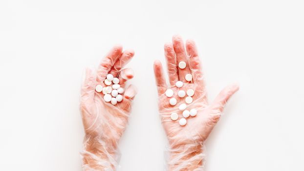 Doctor's palm hands in protective transparent gloves full of white scattering pills. Capsules with medicines on white background with copy space. Flat lay, top view.