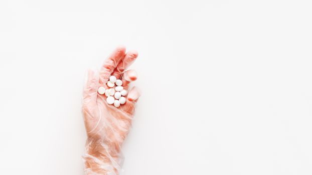 Doctor's palm hand in protective transparent glove full of white scattering pills. Capsules with medicines on white background with copy space. Flat lay, top view.