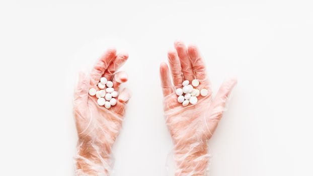 Doctor's palm hands in protective transparent gloves full of white scattering pills. Capsules with medicines on white background with copy space. Flat lay, top view.