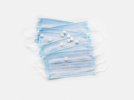 Top view on pack of blue protective medical masks and white scattered pills. Coronavirus COVID-19 concept on white background.