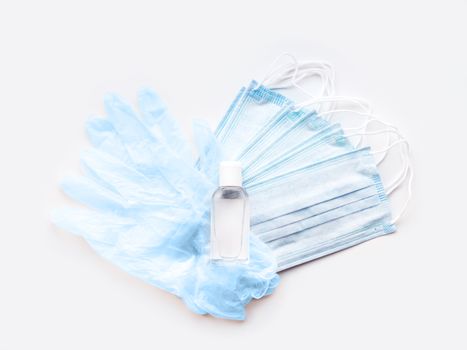 Top view on pack of blue medical masks, protective rubber gloves and transparent bottle with sanitizer gel. Heart shape. Coronavirus COVID-19 concept on white background.