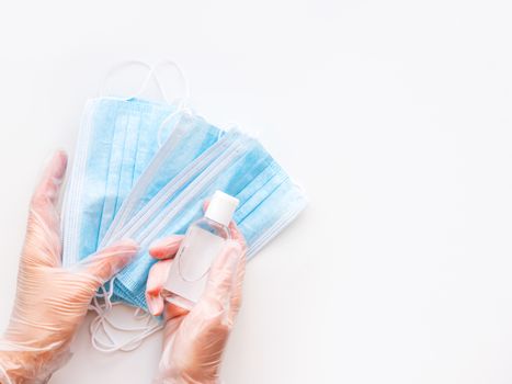 Top view on doctor's hands in protective gloves with medical masks and sanitizer in transparent bottle. Coronavirus COVID-19 concept on white background with copy space.