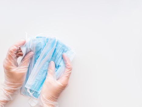 Top view on doctor's hands with pack of blue protective medical masks. Coronavirus COVID-19 concept on white background with copy space.