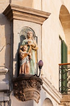 Statue of woman and child on corner of building. Latin inscription is a request to Saint Anne to pray for her worshippers. Malta.