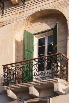 Old fashioned balcony with Maltese cross under metal railings with floral ornament. Traditional architectural detail for buildings in Malta.