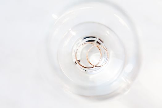 Top view on golden wedding rings inside wine glass. Sun shines through transparent glass.