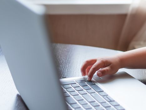 Child explores silver metal laptop. Curious toddler boy presses buttons.