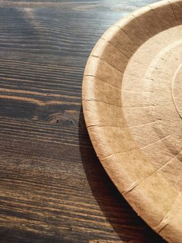 Disposable tableware on wooden table in cafe. Round cardboard plate.