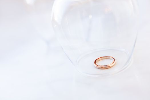 Golden wedding rings under transparent wine glass. Symbol of love and marriage.