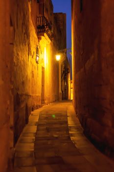 Narrow streets of Mdina, ancient capital of Malta. Night view on illuminated buildings and wall decorations of ancient town.