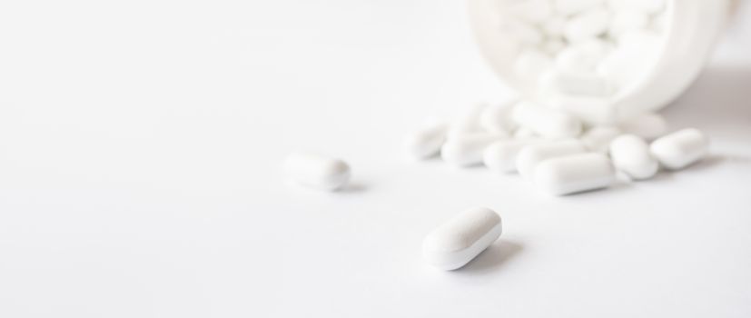 White pills spilled out of a plastic jar. Medicine capsules on white background with copy space.