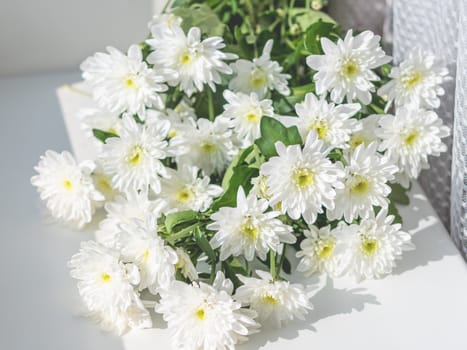 Bouquet of chrysanthemum flowers lying on white window sill. Sunny morning in cozy home.