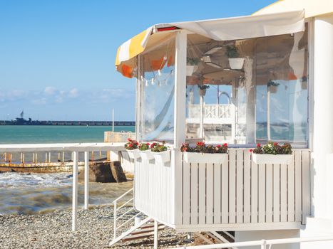 Cafe with views of Black sea and rocky beach. Balcony of white boards with flower beds at plastic windows. Sochi, Russia.