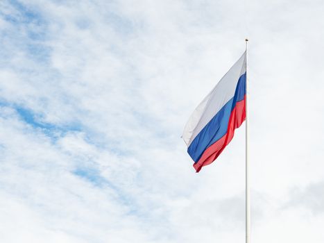 National Russian flag waving on cloudy blue sky background.