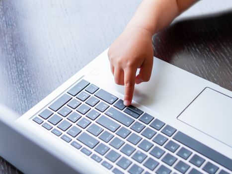 Child explores silver metal laptop. Curious toddler boy presses buttons.