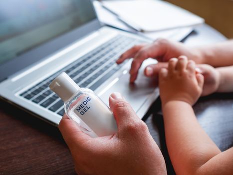 Self-isolation because of coronavirus outbreak. Hand with medical sanitizer gel for skin sterilization. Man is remote working with his little son. Laptop on table.