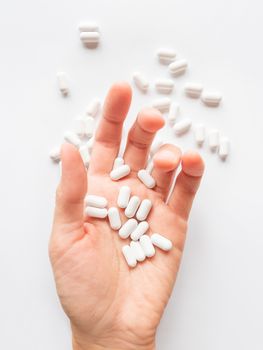 Palm hand full of white scattering pills. Capsules with medicines on light background. Flat lay, top view.