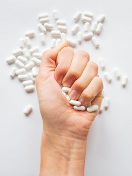 Palm hand full of white scattering pills. Woman gripes hand with capsules with medicines on light background. Flat lay, top view.