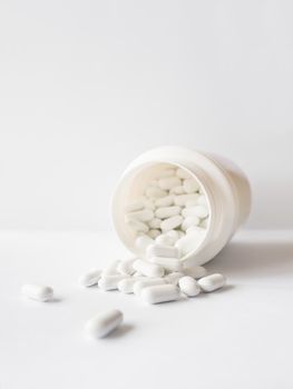 White pills spilled out of a plastic jar. Medicine capsules on white background with copy space.
