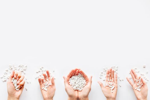 Palm hands full of white scattering pills. Woman gripes hand with capsules with medicines on light background. Flat lay, top view.