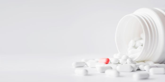 White pills with red one spilled out of a plastic jar. Medicine capsules on white background with copy space.