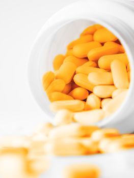 Orange pills spilled out of a plastic jar. Medicine capsules on white background.