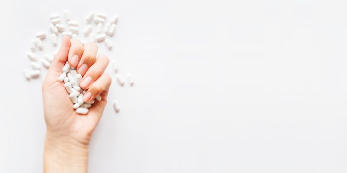 Palm hand full of white scattering pills. Woman gripes hand with capsules with medicines on light background. Flat lay, top view. Banner with copy space.