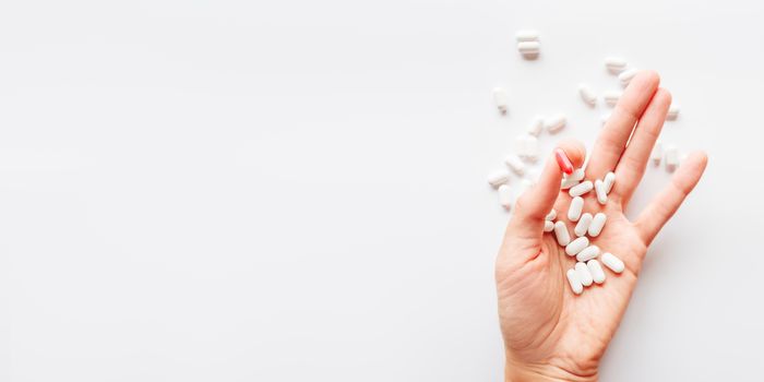 Palm hand full of white and red one scattering pills. Capsules with medicines on light background. Flat lay, top view.