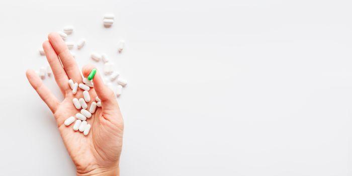 Palm hand full of white and green one scattering pills. Capsules with medicines on light background. Flat lay, top view.