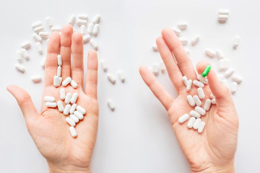 Palm hands full of white and green one scattering pills. Capsules with medicines on light background. Flat lay, top view.