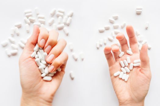 Palm hands full of white scattering pills. Woman gripes hand with capsules with medicines on light background. Flat lay, top view.