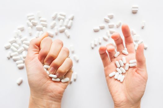 Palm hands full of white scattering pills. Woman gripes hand with capsules with medicines on light background. Flat lay, top view.