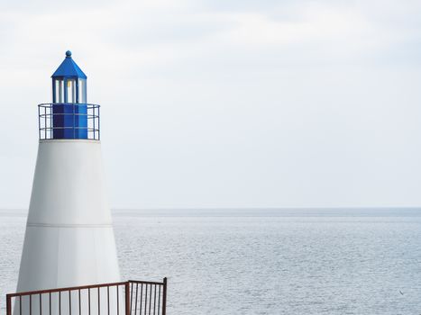 White lighthouse with blue tower on grey tranquil sea background. Natural background with copy space.