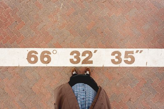 Tourist man taking photoof his feet next to the coordinates of the Arctic circle written on the asphalt. Rovaniemi, Finland.