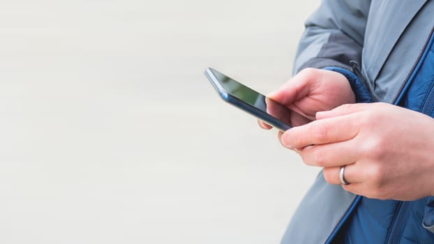 Man's hands with smartphone. Man is texting to somebody. Background with copy space.