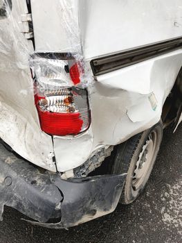 Car after the accident. Broken bumper and headlight. White car with dents covered with plastic wrap.