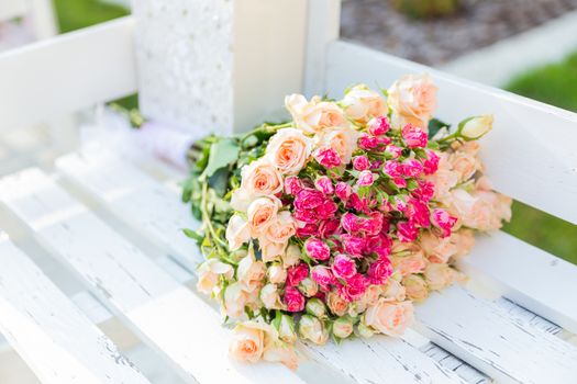 Bouquet with roses on white bench. Colorful flowers, traditional floral composition for wedding ceremony.