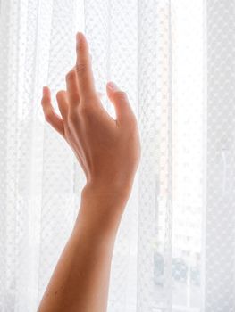 Graceful woman hand on tulle curtains background. Sun lights through window.