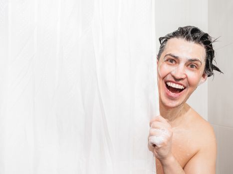 Young man in soap suds looks out from behind a curtain in the bathroom. Man was taking a shower.