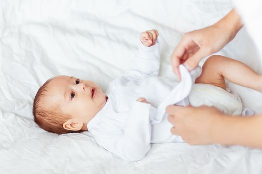 Mother changes the child's clothes. Woman changes a bodysuit for a young son or daughter.