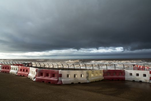 Red and white plastic safety barriers line the sea front as a storm approches.