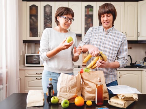 Young couple is sorting out purchases in the kitchen. Products in bags made of craft paper. Food delivery in conditions of quarantine because of coronavirus COVID19.