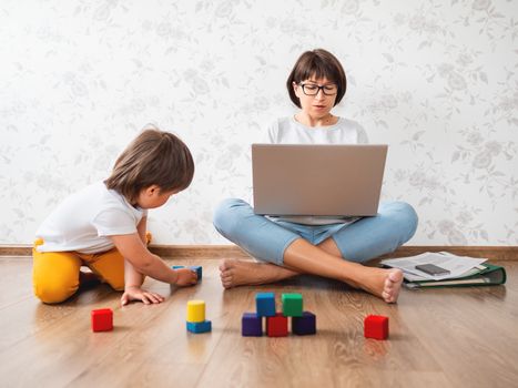 Mom and son argue at home quarantine because of coronavirus COVID19. Mother remote works with laptop, son plays with toy blocks. Self isolation at home.