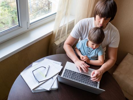 Self-isolation because of coronavirus outbreak. Man is remote working with his little son on self quarantine. Lockdown.