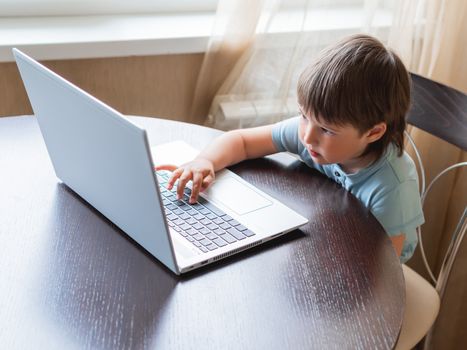 Curious toddler boy explores the laptop and presses buttons on computer keyboard.