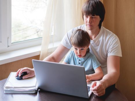 Self-isolation because of coronavirus outbreak. Man is remote working with his little son on self quarantine. Lockdown.