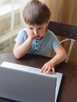 Curious toddler boy explores the laptop and presses buttons on computer keyboard.