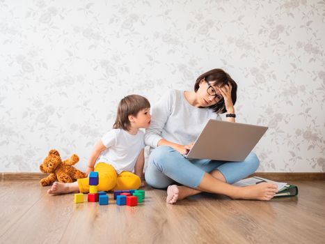 Mom and son sit at home quarantine because of coronavirus COVID19. Mother remote works with laptop, son plays with toy blocks. Self isolation at home.